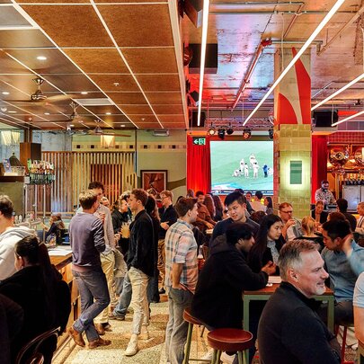 A busy colourful bar with people watching sport.