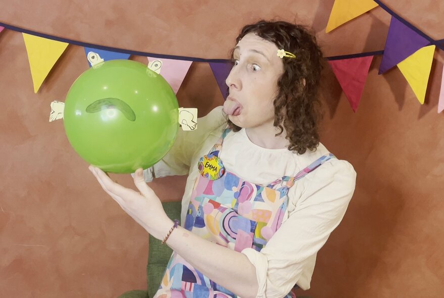 Children's entertainer holding a green balloon and sticking out their tongue.
