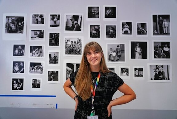 The curator Savannah Smith in front of a wall-mounted collection of black-and-white portraits for an exhibition.