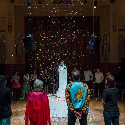 People standing in a circle around a central figure with confetti raining down.