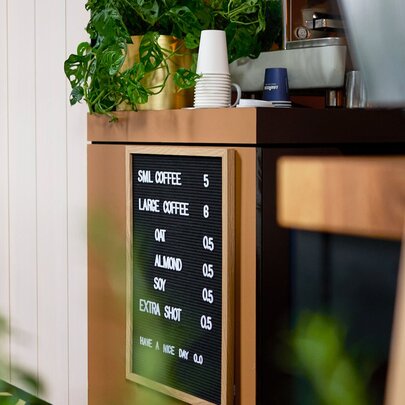 The coffee counter with green plants and a simple undecipherable coffee menu attached to the counter's side.