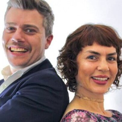 Jazz vocalists Jackie Bornstein and Jeremy Hopkins pose together back to back in front of a white backdrop. 
