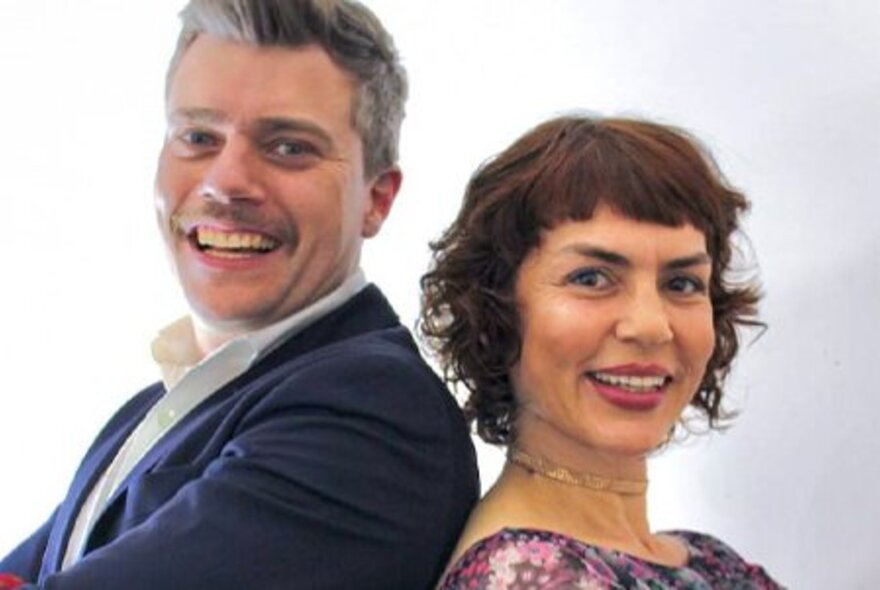Jazz vocalists Jackie Bornstein and Jeremy Hopkins pose together back to back in front of a white backdrop. 