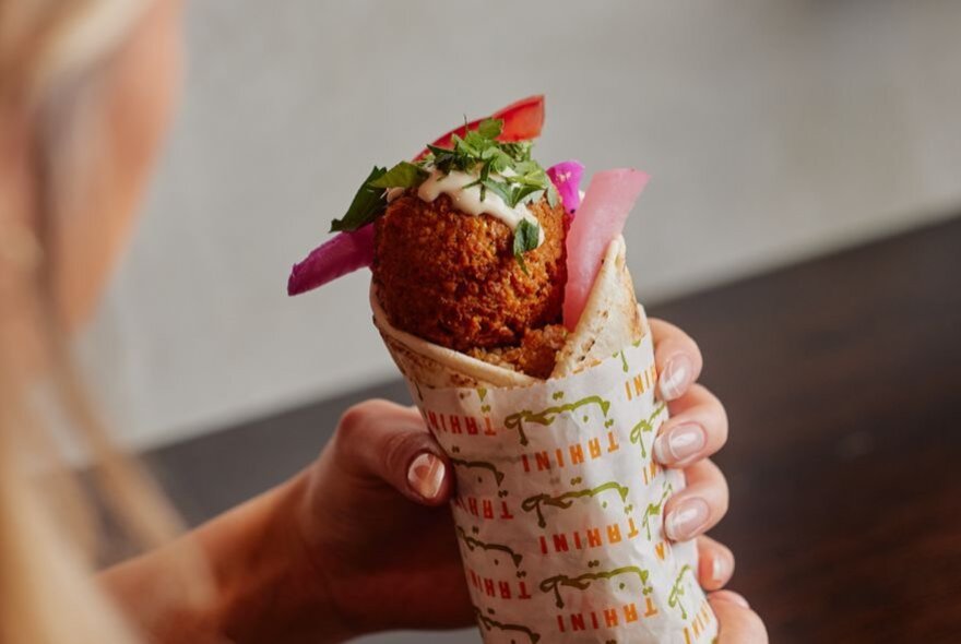 A woman's hand holding a Lebanese falafel wrap.