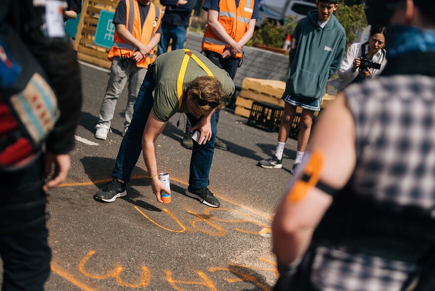 Game participants painting words on the ground with orange spraypaint.