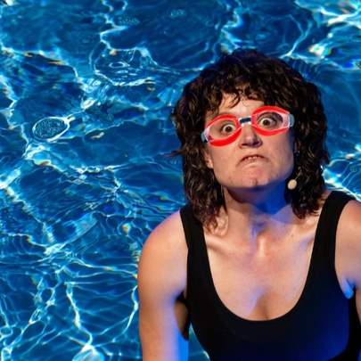 Woman wearing red goggles and a frowning expression in a swimming pool.
