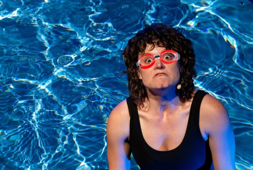 Woman wearing red goggles and a frowning expression in a swimming pool.