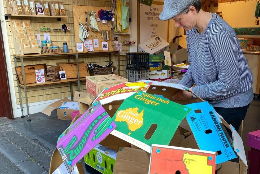 Person making a globe made from cardboard boxes in a shop with products on shelves.