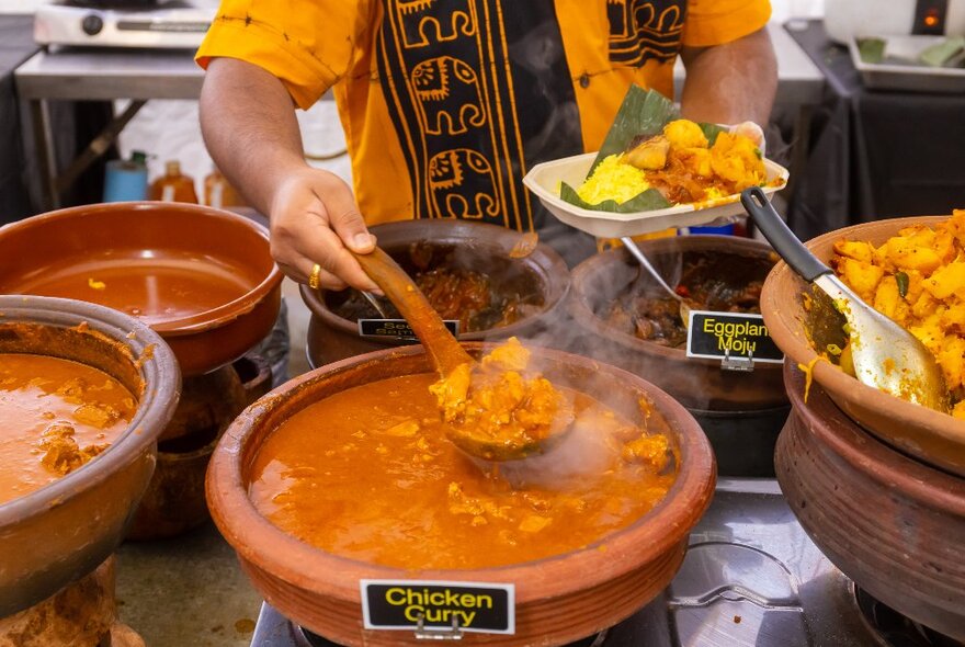 Someone dishing up chicken curry onto a banana leaf at a market stall.