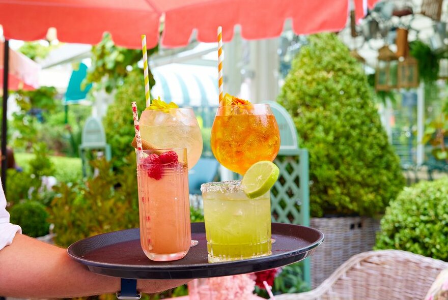 A tray full of colourful cocktails in a beer garden.