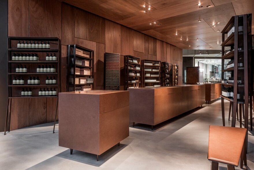 The timber interior of an Aesop shop with products on shelves lining the walls and large wooden block tables. 