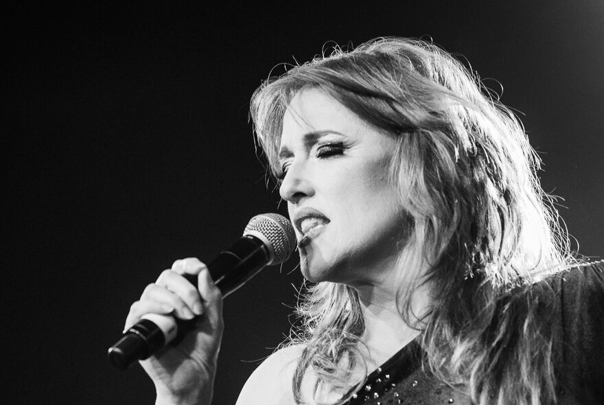 Performer Geraldine Quinn singing into a microphone she is holding, eyes closed; black and white image.