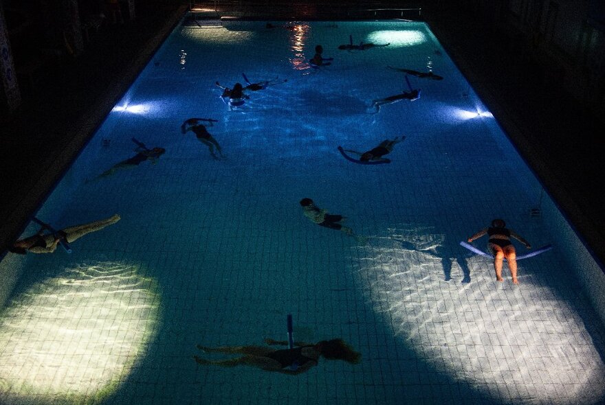 People floating in a darkened swimming pool, listening to underwater music.