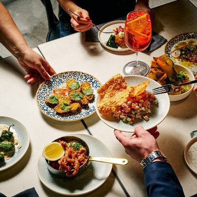 Hands reaching over a table to serve up food from a selection of share plates.