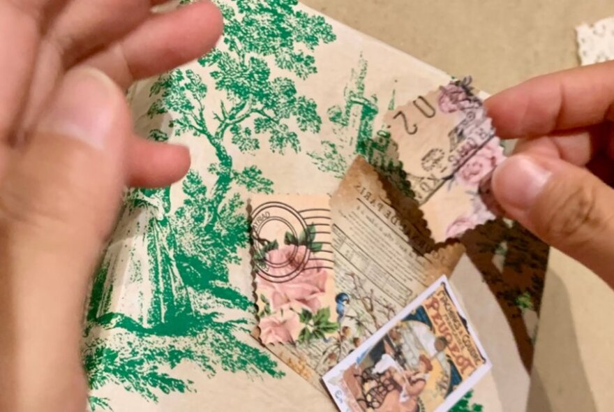 Hands holding a box covered in patterned paper, adding stamps.