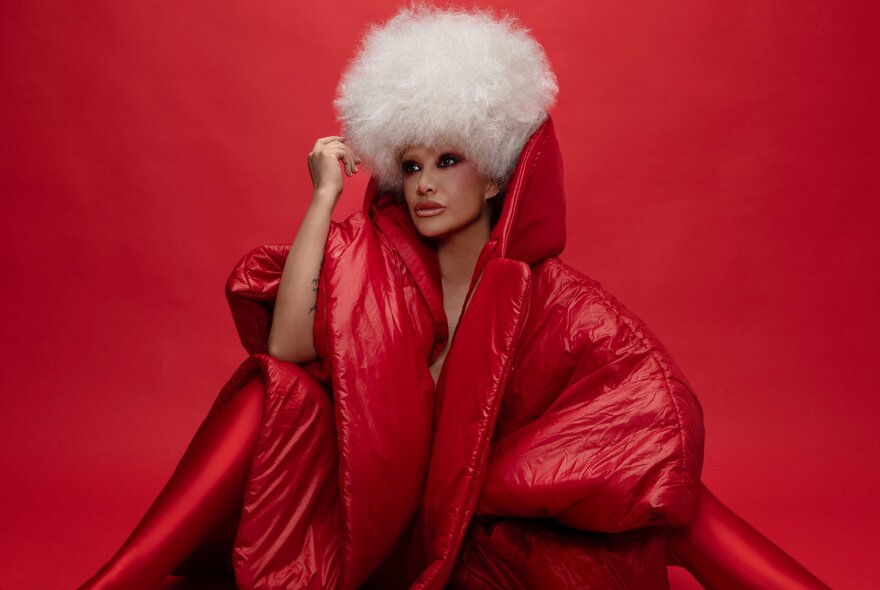 Jazz singer Lady Blackbird in a white curly wig and puffy red outfit with an exaggerated collar turned up. 
