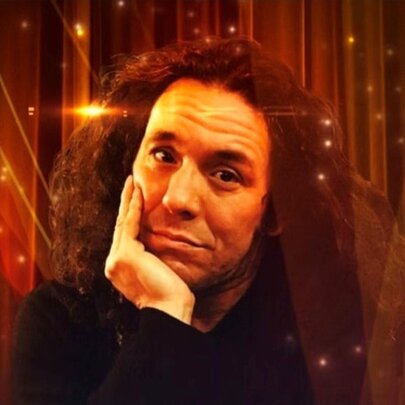 Magician Hernan Maccagno, resting his head on his hand, a glittering stage curtain behind him.
