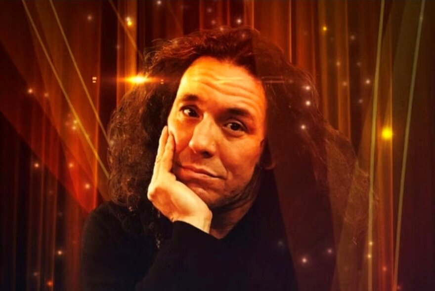 Magician Hernan Maccagno, resting his head on his hand, a glittering stage curtain behind him.