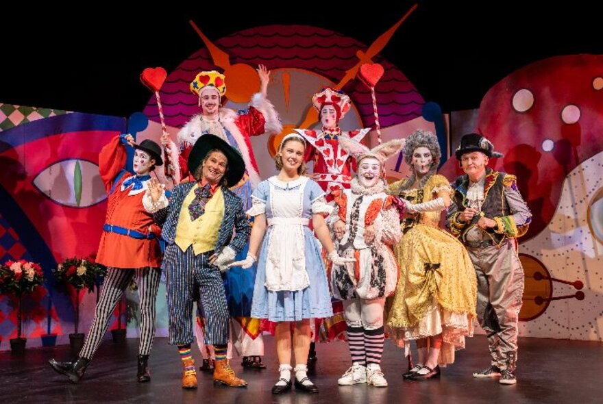 The cast of Alice in Wonderland, in costume, standing in a group together on a theatre stage.  