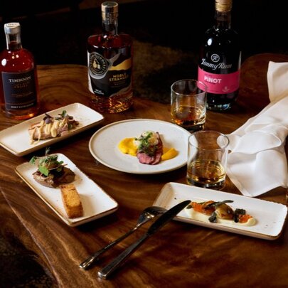 A wooden table in a restaurant with bottles of wine and plates of food.
