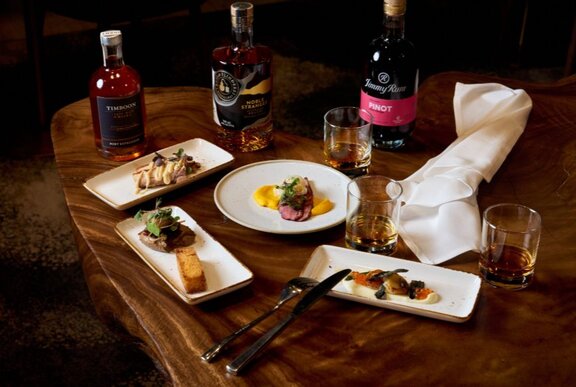 A wooden table in a restaurant with bottles of wine and plates of food.