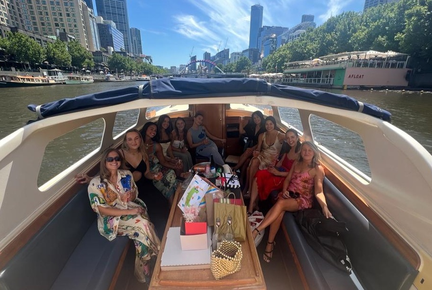 People seated in a water taxi cabin gliding on the Yarra River.