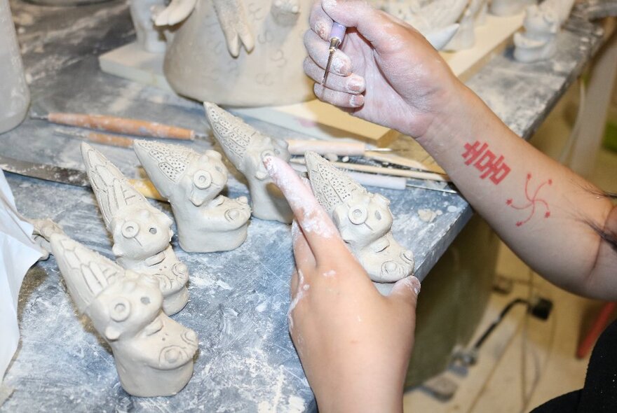 Hands forming clay models of gnomes at a workbench.