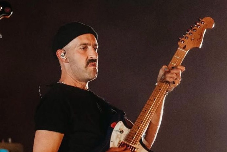 A man wearing a black beanie and a black t-shirt playing an electric guitar.