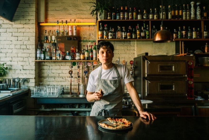 A chef posing with a pizza in a moody bar enviroment. 