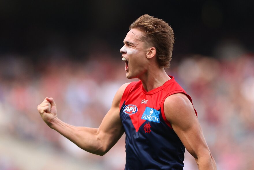 A Melbourne AFL player with a pumped fist and cheering himself and the crowd on during a match.