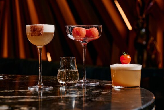 Four tomato-based cocktails in four different shaped cocktail glasses, on a dark marble table.