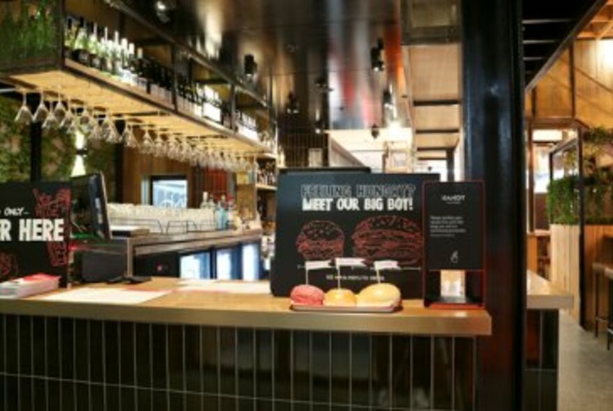 A counter at a bar with burgers lined up. 