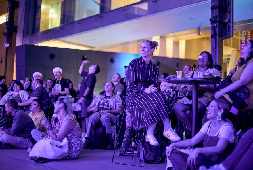 An audience attending an evening performance or talk, seated at tables or on the floor, as part of Nocturnal at Melbourne Museum.