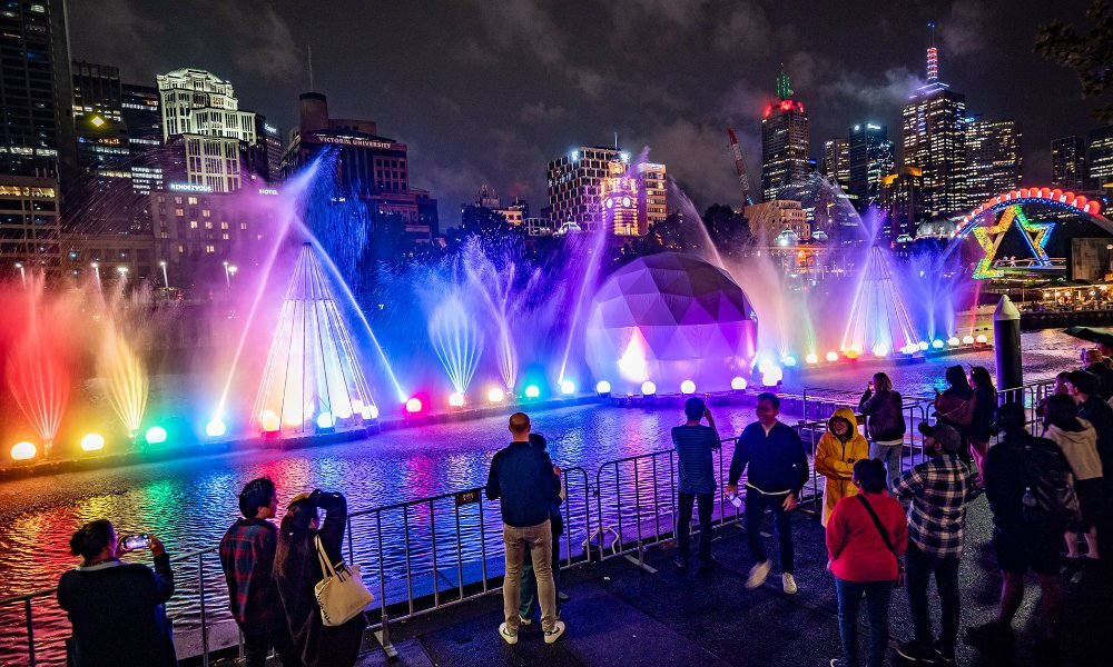 People watching a colourful river light show at night.