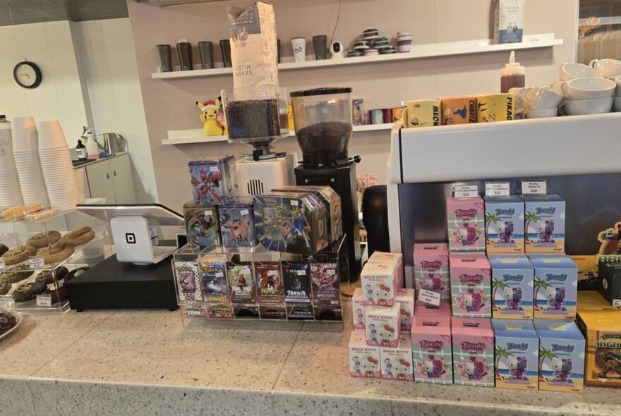 Counter of a cafe with a coffee machine, takeaway coffee cups, and products displayed for sale.