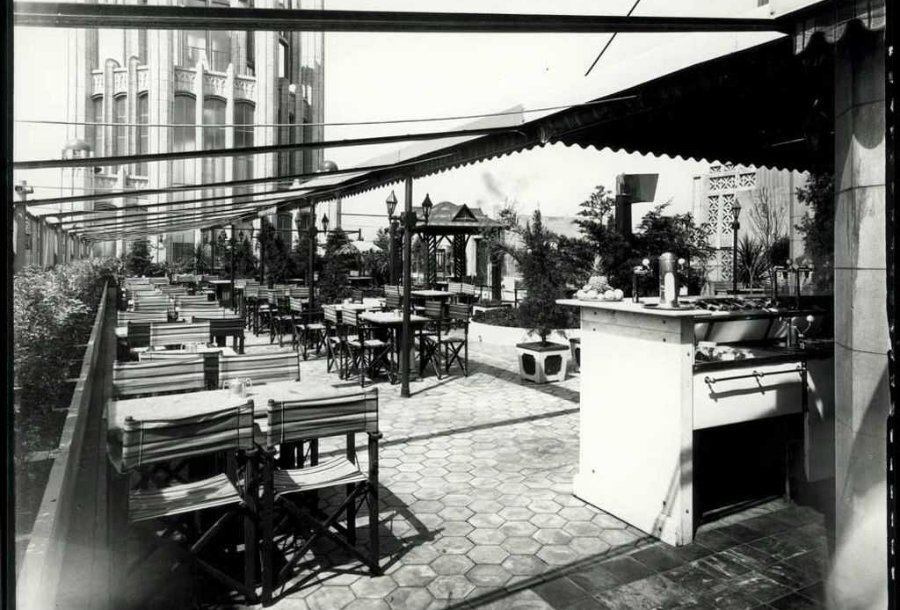 A black and white photo of an empty outdoor terrace at a cafe with dining tables 