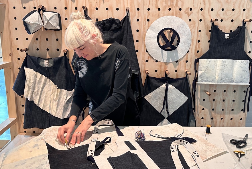 A person with platinum blonde hair working on a project using fabric in a workshop environment. 