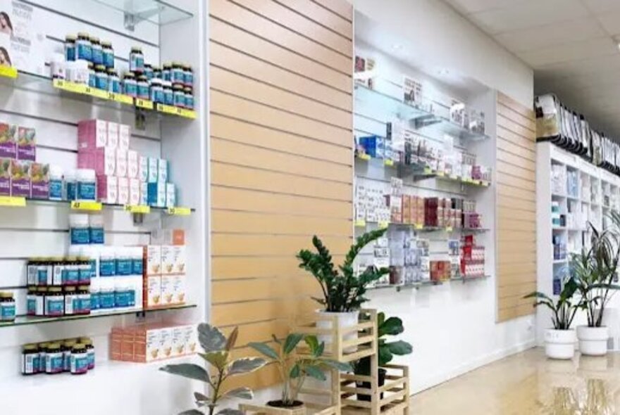 Interior of a retail space, with products displayed on shelves on a wall, green plants in pots and a shiny timber floor.