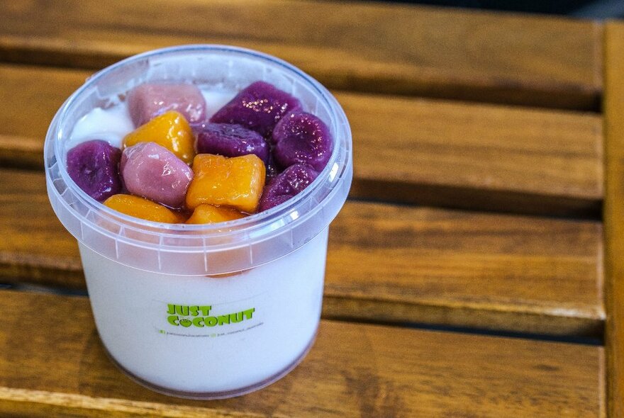 A small coconut and diced fruit cup on a wooden stool, from the cafe Just Coconut.