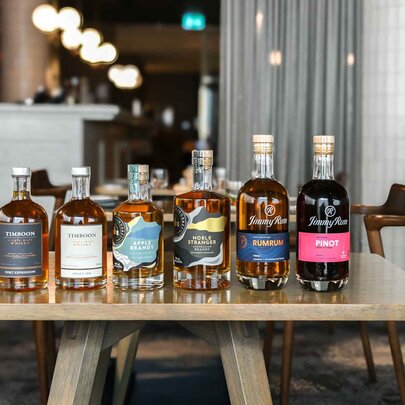 A wooden table in a restaurant with six spirit bottles lined up along one edge.