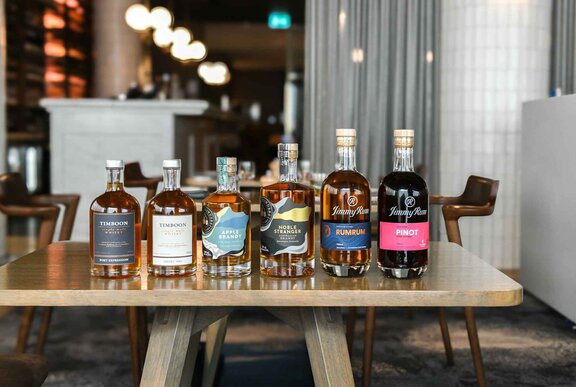 A wooden table in a restaurant with six spirit bottles lined up along one edge.