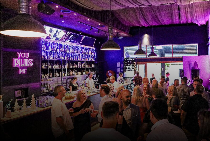 The interior of a bar with patrons standing at bar tables and ordering drinks at the bar.