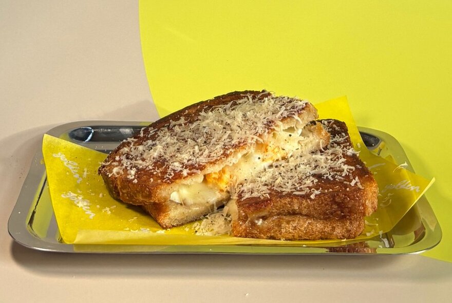 A melting cheese toastie on a silver tray with serviette.