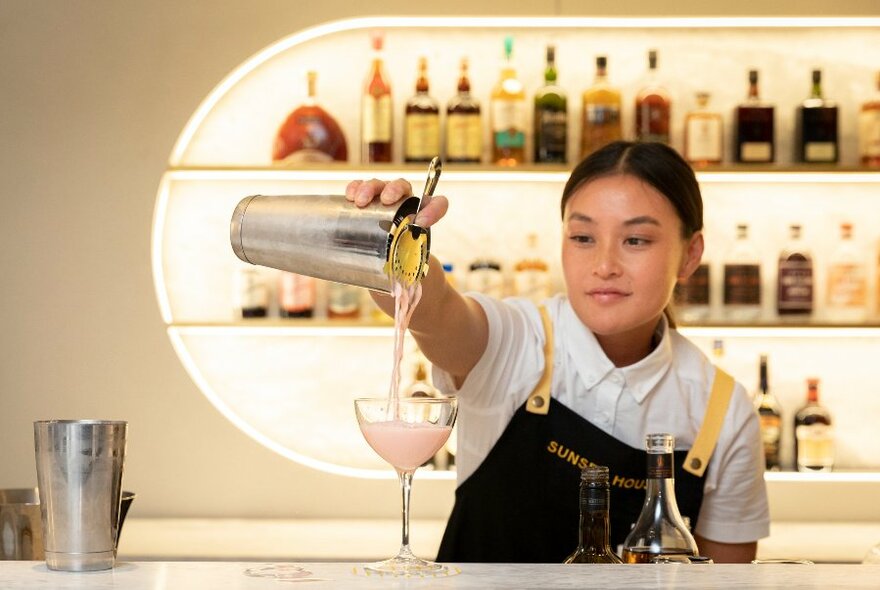 A bartender pours a pink cocktail from a shaker. 