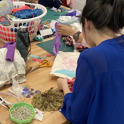 Looking over the shoulder of a woman at a cluttered craft table. 