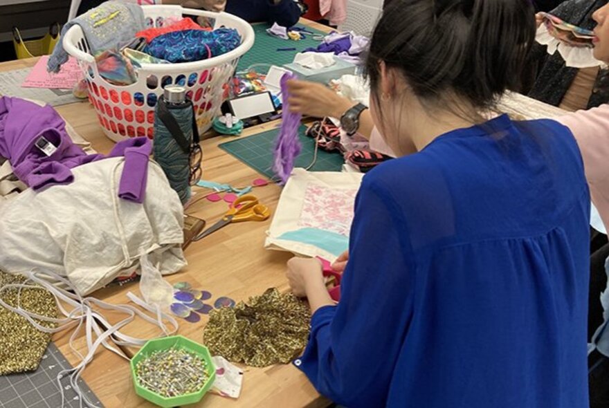 Looking over the shoulder of a woman at a cluttered craft table. 