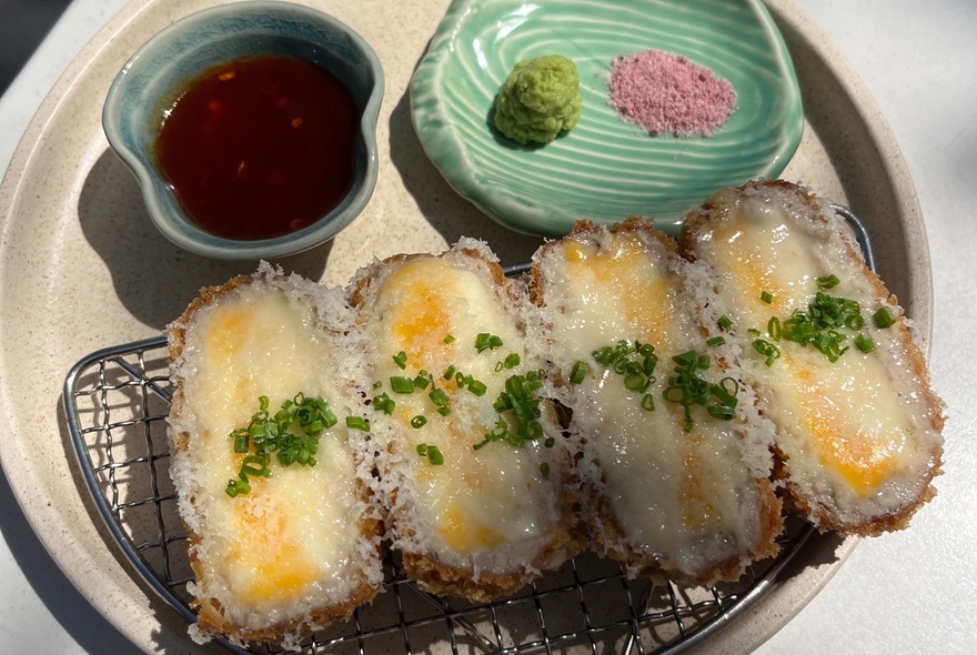  Crumbed katsu on a wire tray with dipping sauce and condiments.