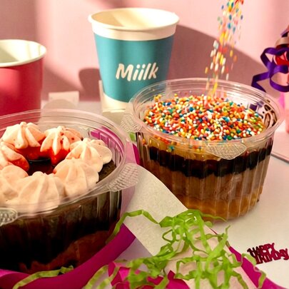 Two cakes in plastic cups with colourful toppings, surrounded by party decorations.