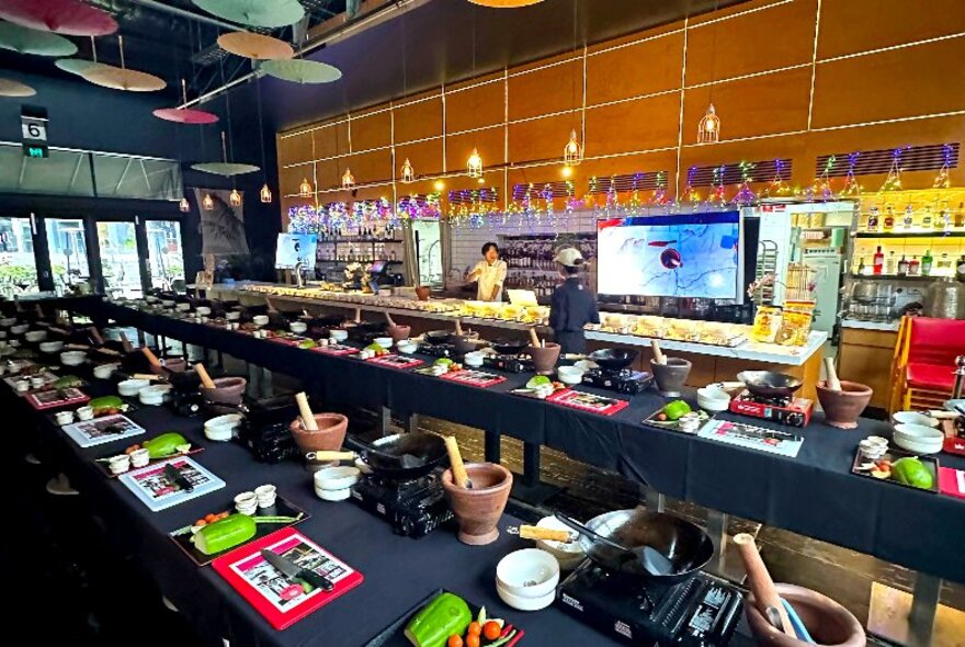 Long tables set up with cooking stations and ingredients and cooking utensils, ready for a Thai cooking workshop.