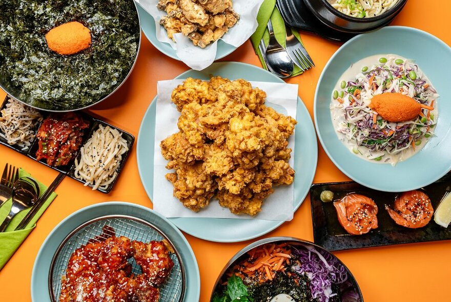 Looking down on a table laden with Korean food of various kinds - fried chicken in the centre. 